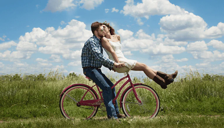 Foto de um casal andando de bicicleta em um campo aberto.