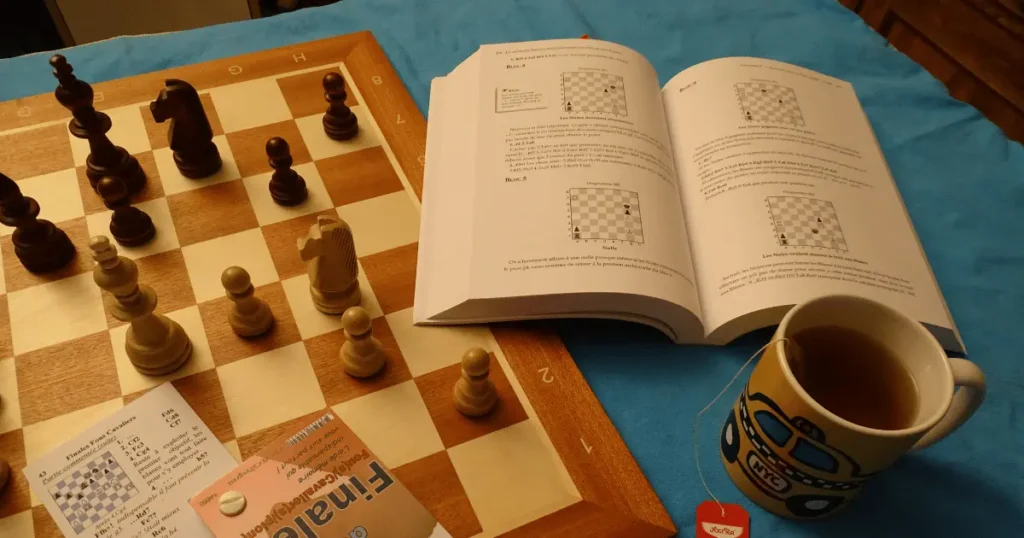 Tabuleiro de xadrez com livros sobre xadrez abertos e uma xícara de chá ao lado