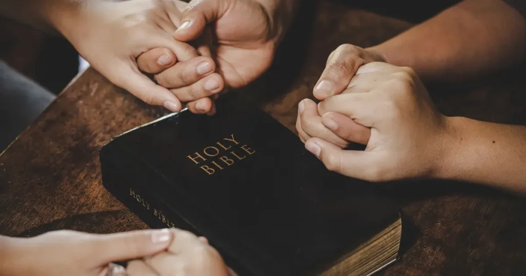 Jovens de mãos dadas em oração ao redor de uma Bíblia aberta, simbolizando os valores e ensinamentos presentes nos melhores livros cristãos para jovens.