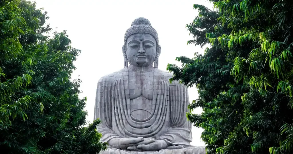 Grande estátua de Buda em postura de meditação cercada por árvores, representando a serenidade e os ensinamentos presentes nos melhores livros sobre budismo.